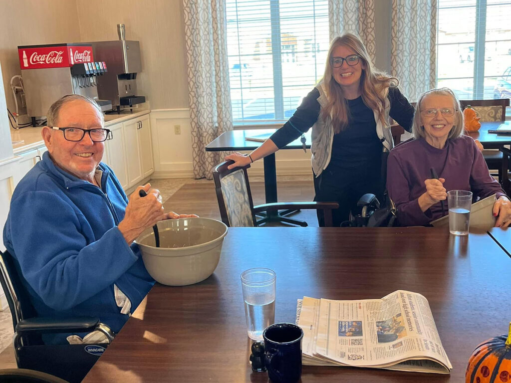 Memory care residents happily bake with volunteers in a cozy kitchen.