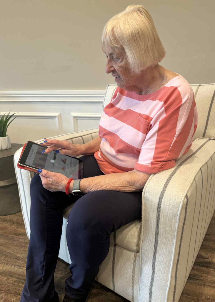 Senior resident seated in a striped chair engages with the Arrow app on a tablet, navigating its features with focus and confidence.