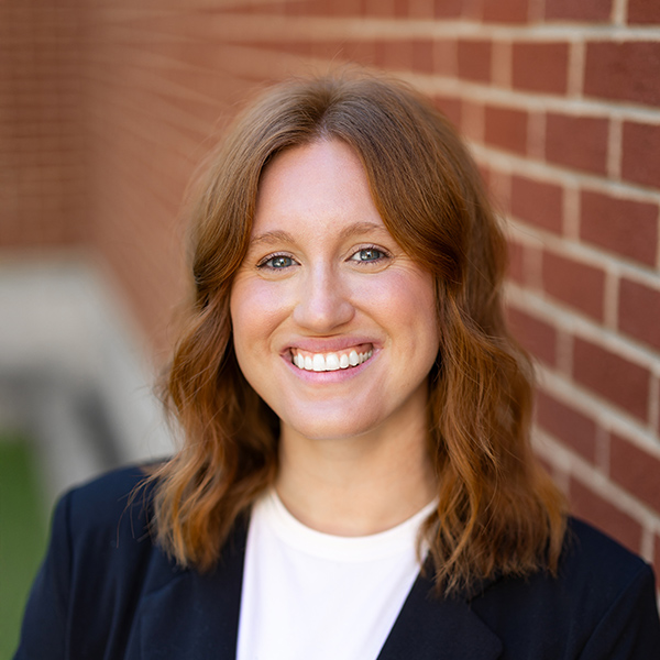Emily Chuppa, Business Office Director at Vitalia North Royalton, smiling in a professional headshot, wearing a dark blazer and white top, standing beside a red brick wall with a softly blurred background.