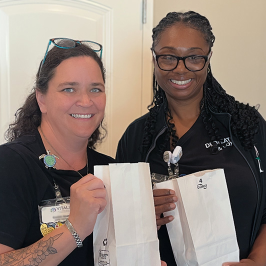 Two women on the team at Vitalia North Royalton smile, holding gift bags.