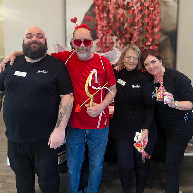 Four team members smile, some wearing valentine's props and holding treats.