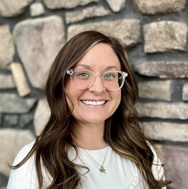 Melanie Knautz, Wellness Director at Vitalia North Royalton, smiling in a professional headshot, wearing glasses and a light top, with a softly blurred stone wall background.