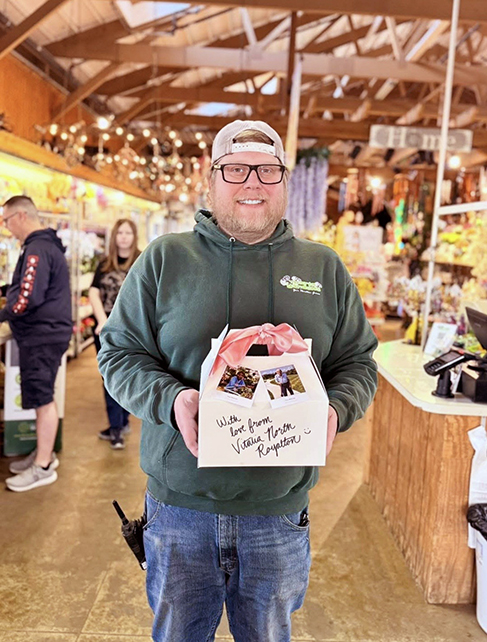 A local business owner smiles in his establishment, among high ceilings, woodwork, and warm lighting, holding a gift from Vitalia North Royalton.
