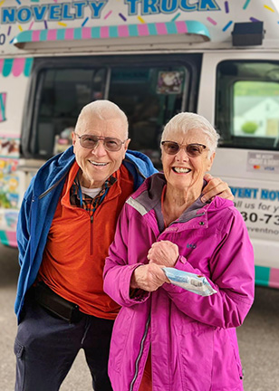 A senior man and woman from Vitalia North Royalton smile brightly in front of a colorful ice cream truck.